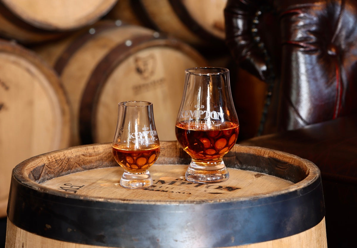 Two glasses of whisky on a wooden barrel with barrels in the background